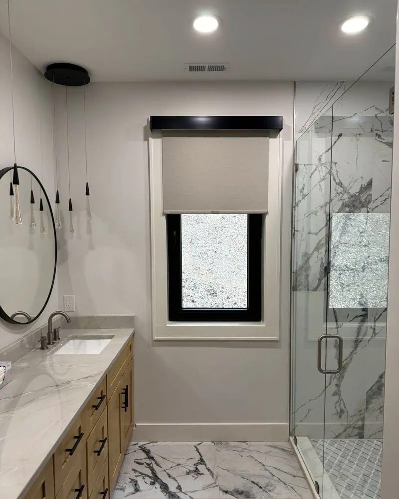 Roller shade with a black cassette on a bathroom window beside a glass shower