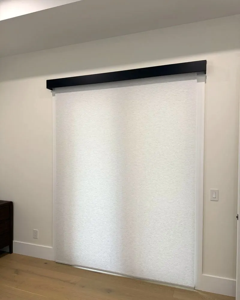 Wide light filtering roller shade lowered over a patio door