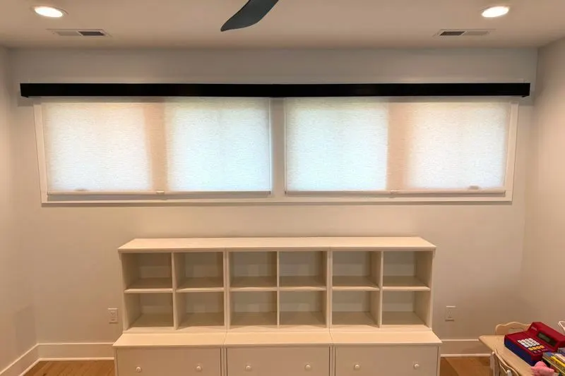 Four roller shades under one valance above a built-in bookcase